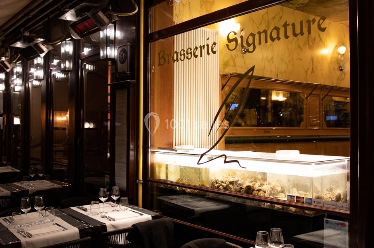 Façade d'une brasserie avec une vitrine éclairée contenant des huîtres et des tables dressées en terrasse.