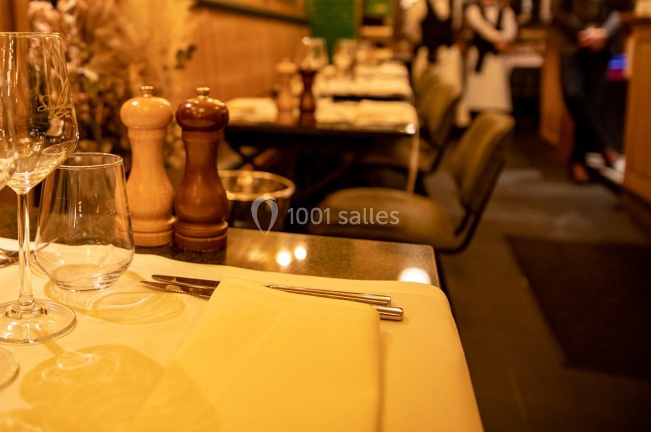 Table dressée avec nappe beige, couverts, verres et moulins à épices, dans un restaurant à l'ambiance chaleureuse.
