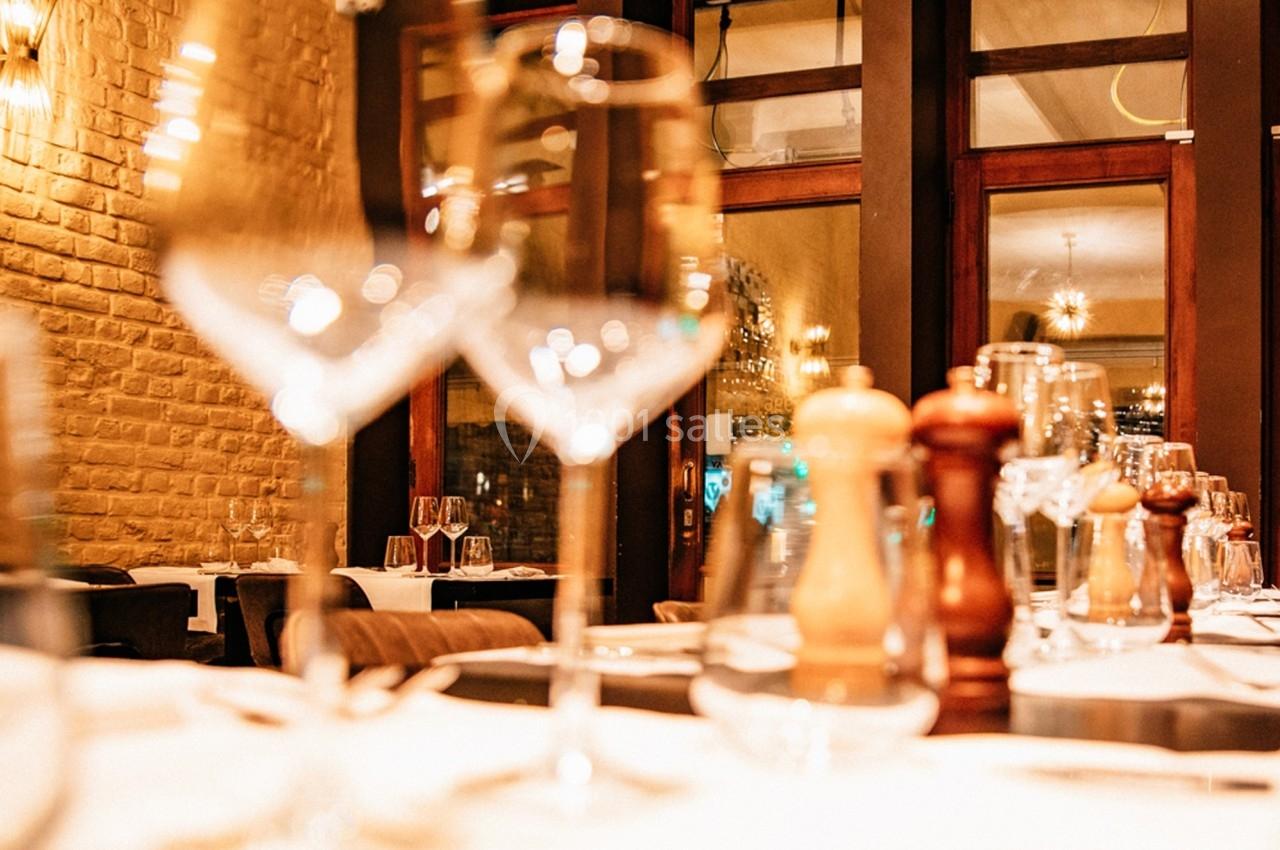 Salle de restaurant élégante avec tables dressées, verres et moulins à épices, éclairage chaleureux.