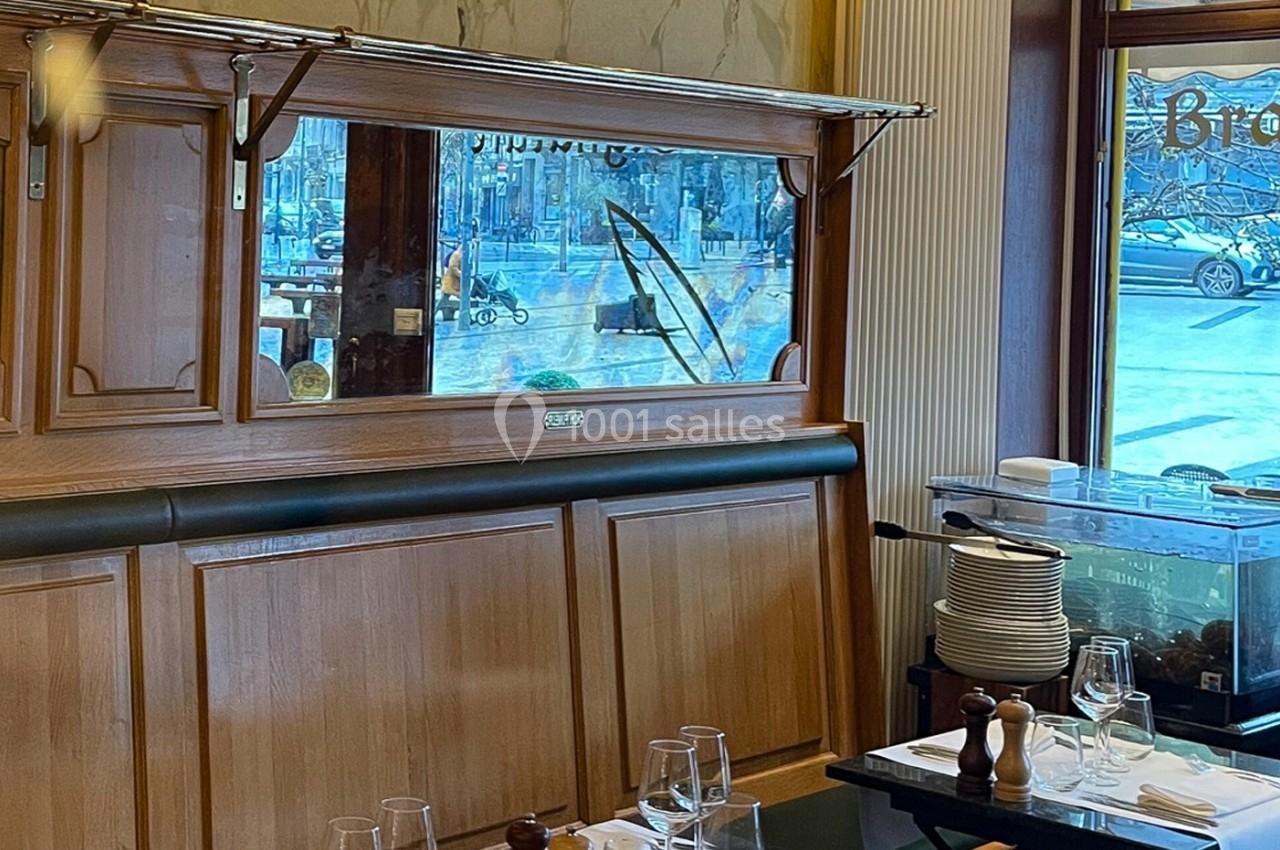 Banquette en bois avec miroir gravé, table dressée avec vaisselle et vue sur une rue à travers la fenêtre.