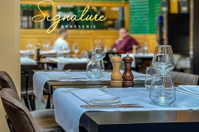 Salle de restaurant avec tables dressées, banquettes en bois, bar en bois et étagères garnies de verres et bouteilles.