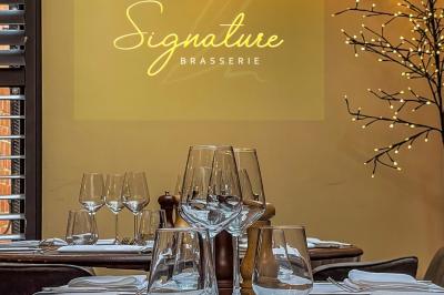 Salle de restaurant avec tables dressées, banquettes en bois, bar en bois et étagères garnies de verres et bouteilles.