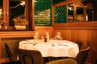 Salle de restaurant avec tables dressées, banquettes en bois, bar en bois et étagères garnies de verres et bouteilles.