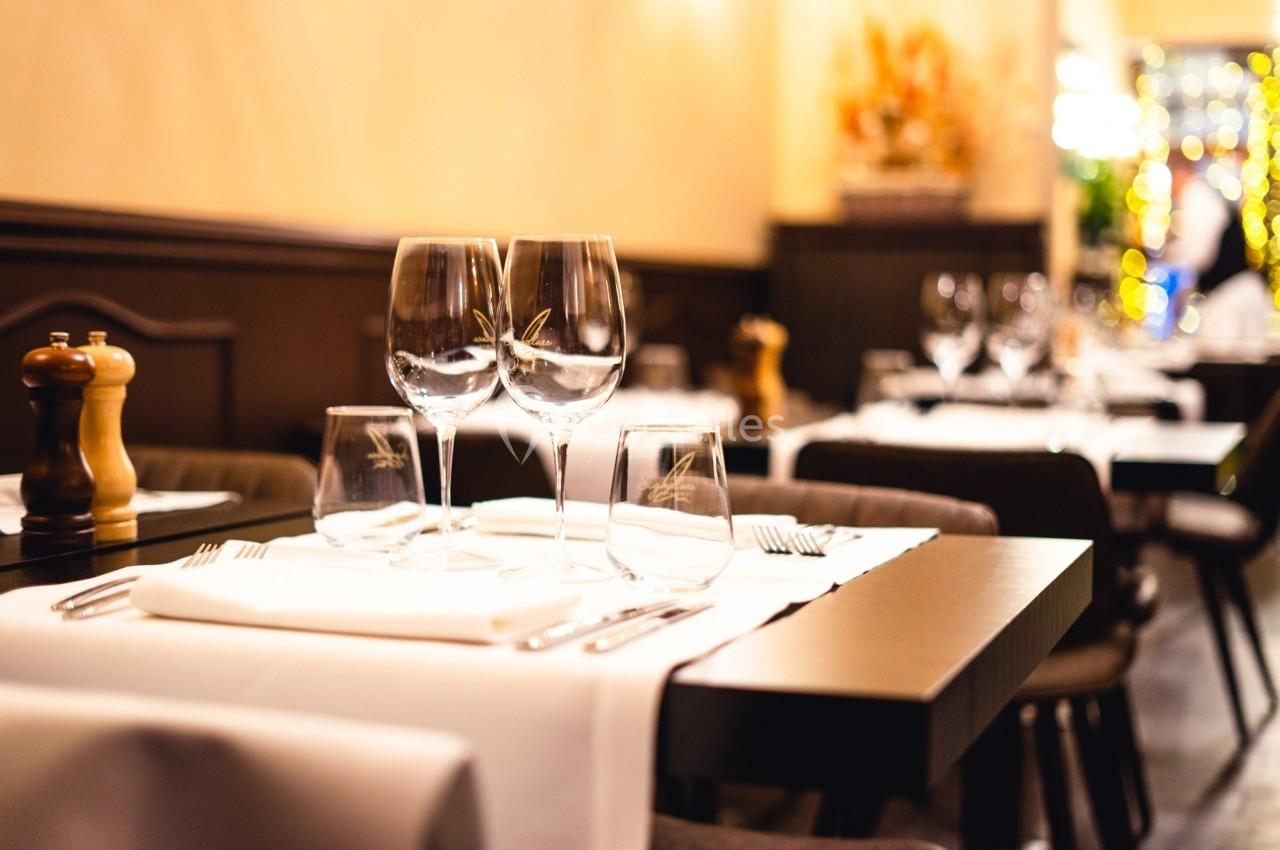 Table de restaurant élégamment dressée avec nappes blanches, verres à vin et couverts, dans une ambiance chaleureuse.