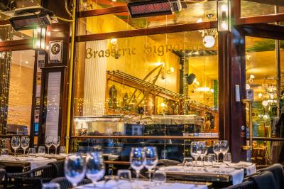 Salle de restaurant avec tables dressées, banquettes en bois, bar en bois et étagères garnies de verres et bouteilles.