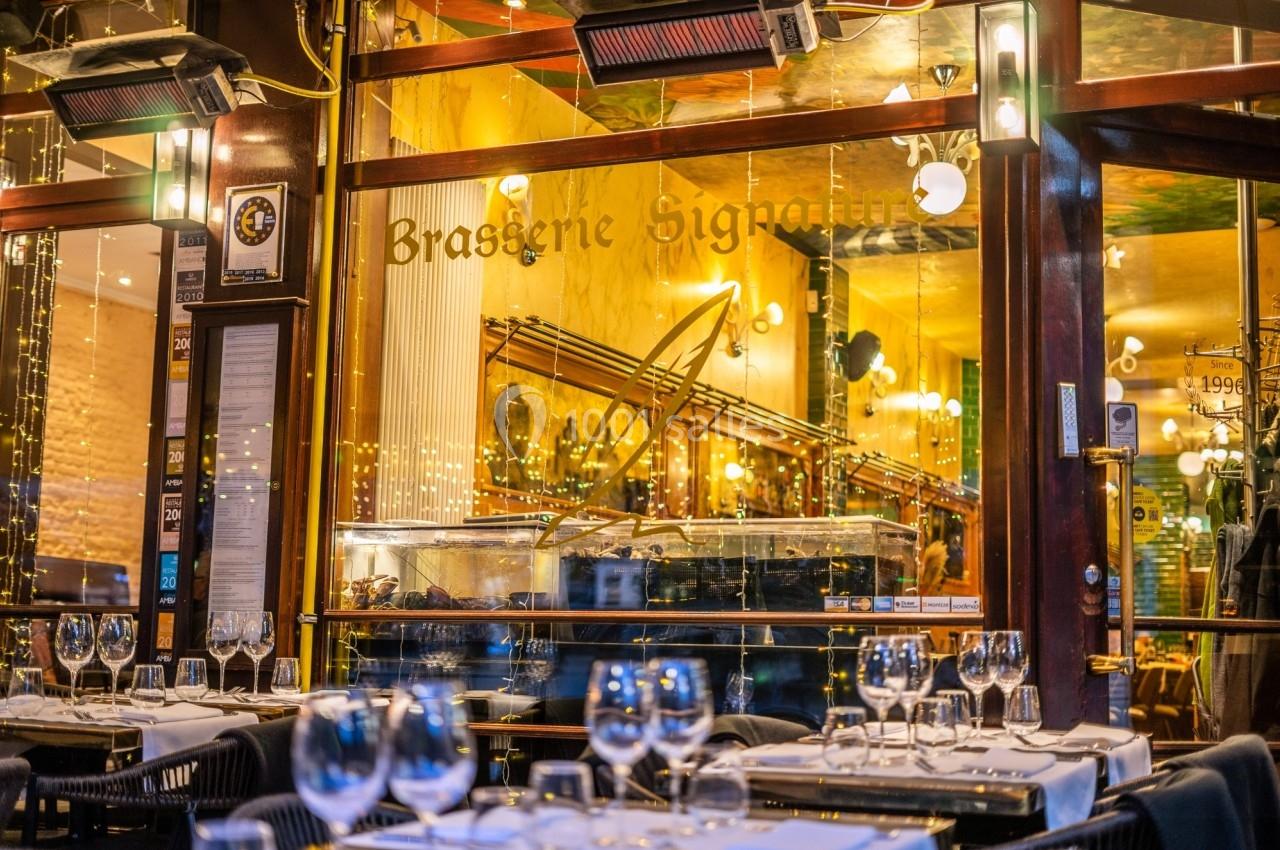 Façade d'une brasserie avec tables dressées en terrasse, éclairage chaleureux et décoration intérieure visible.