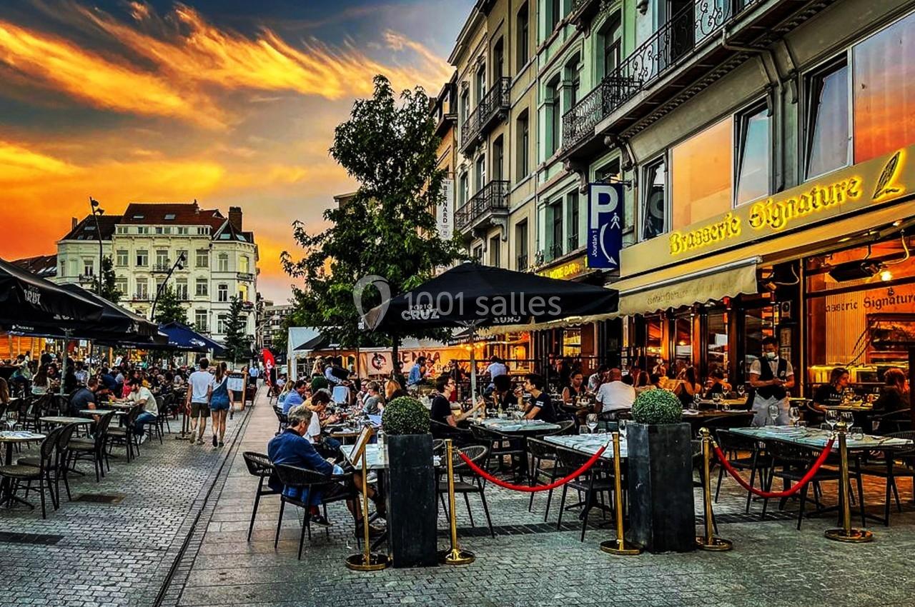 Terrasse animée d'un restaurant en soirée, avec des clients assis sous un ciel coloré au coucher du soleil.