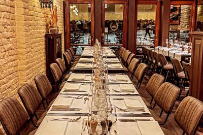 Salle de restaurant avec tables dressées, banquettes en bois, bar en bois et étagères garnies de verres et bouteilles.