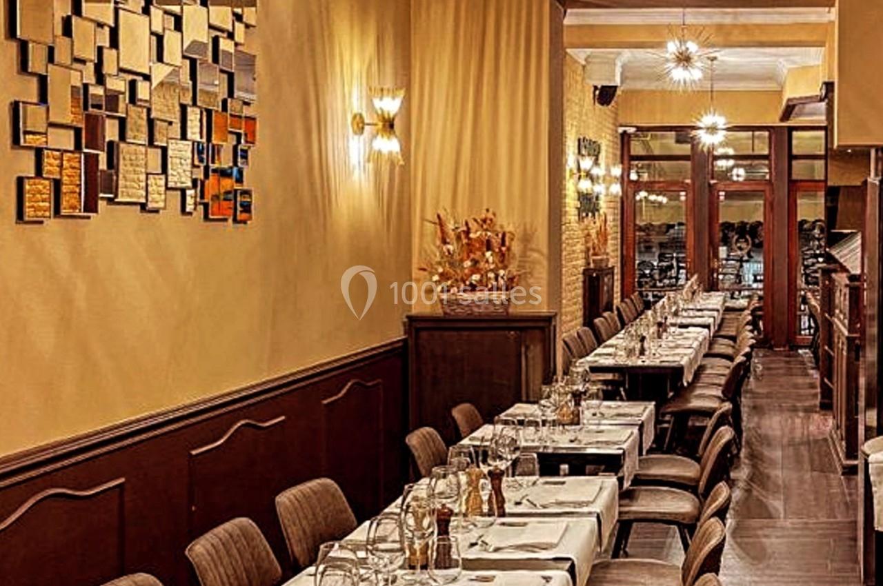 Salle de restaurant élégante avec longues tables dressées, éclairage chaleureux et décoration murale en mosaïque.