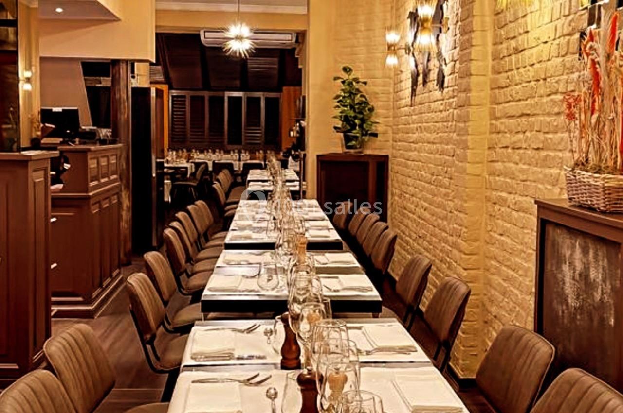 Salle de restaurant avec une longue table dressée, chaises alignées, éclairage chaleureux et décoration murale.