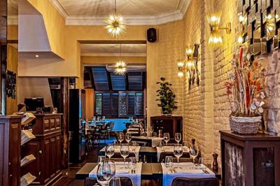 Salle de restaurant avec tables dressées, banquettes en bois, bar en bois et étagères garnies de verres et bouteilles.