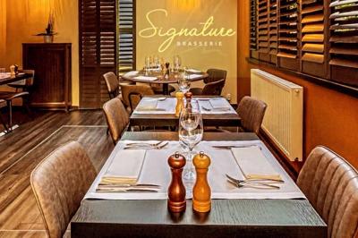 Salle de restaurant avec tables dressées, banquettes en bois, bar en bois et étagères garnies de verres et bouteilles.