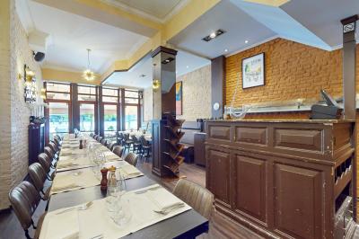 Salle de restaurant avec tables dressées, banquettes en bois, bar en bois et étagères garnies de verres et bouteilles.
