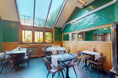 Salle de restaurant avec tables dressées, banquettes en bois, bar en bois et étagères garnies de verres et bouteilles.
