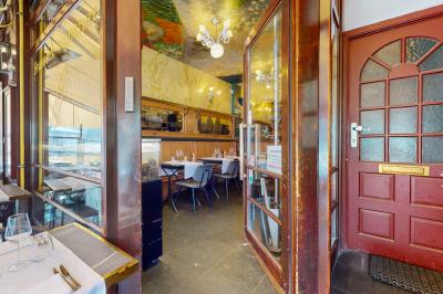 Salle de restaurant avec tables dressées, banquettes en bois, bar en bois et étagères garnies de verres et bouteilles.