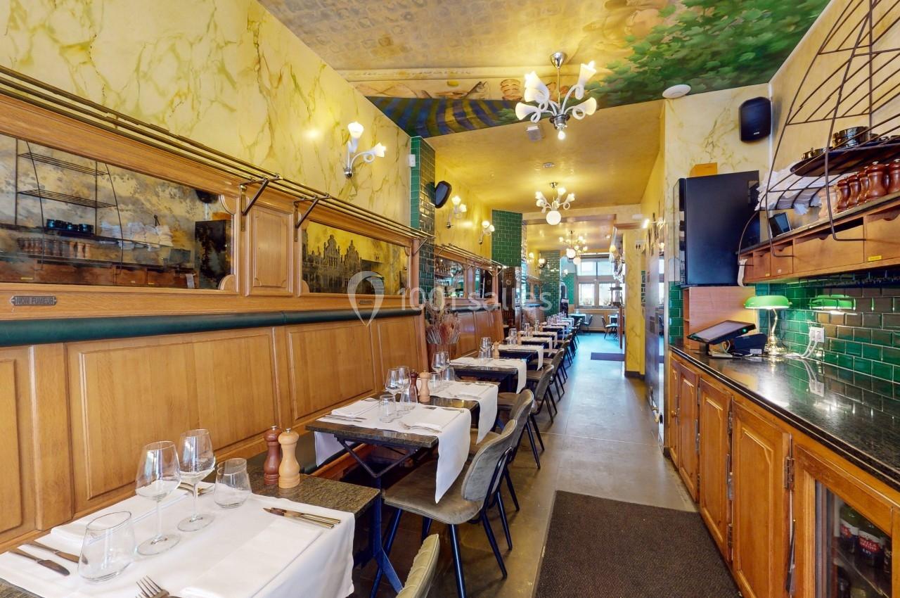 Salle de restaurant étroite avec tables dressées, murs en bois et éclairage chaleureux, vue vers l'entrée.