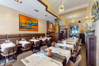 Salle de restaurant avec tables dressées, banquettes en bois, bar en bois et étagères garnies de verres et bouteilles.