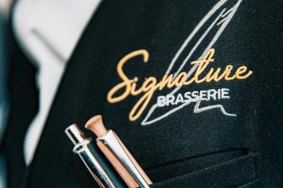 Salle de restaurant avec tables dressées, banquettes en bois, bar en bois et étagères garnies de verres et bouteilles.