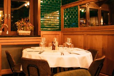 Salle de restaurant avec tables dressées, banquettes en bois, bar en bois et étagères garnies de verres et bouteilles.