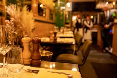 Salle de restaurant avec tables dressées, banquettes en bois, bar en bois et étagères garnies de verres et bouteilles.