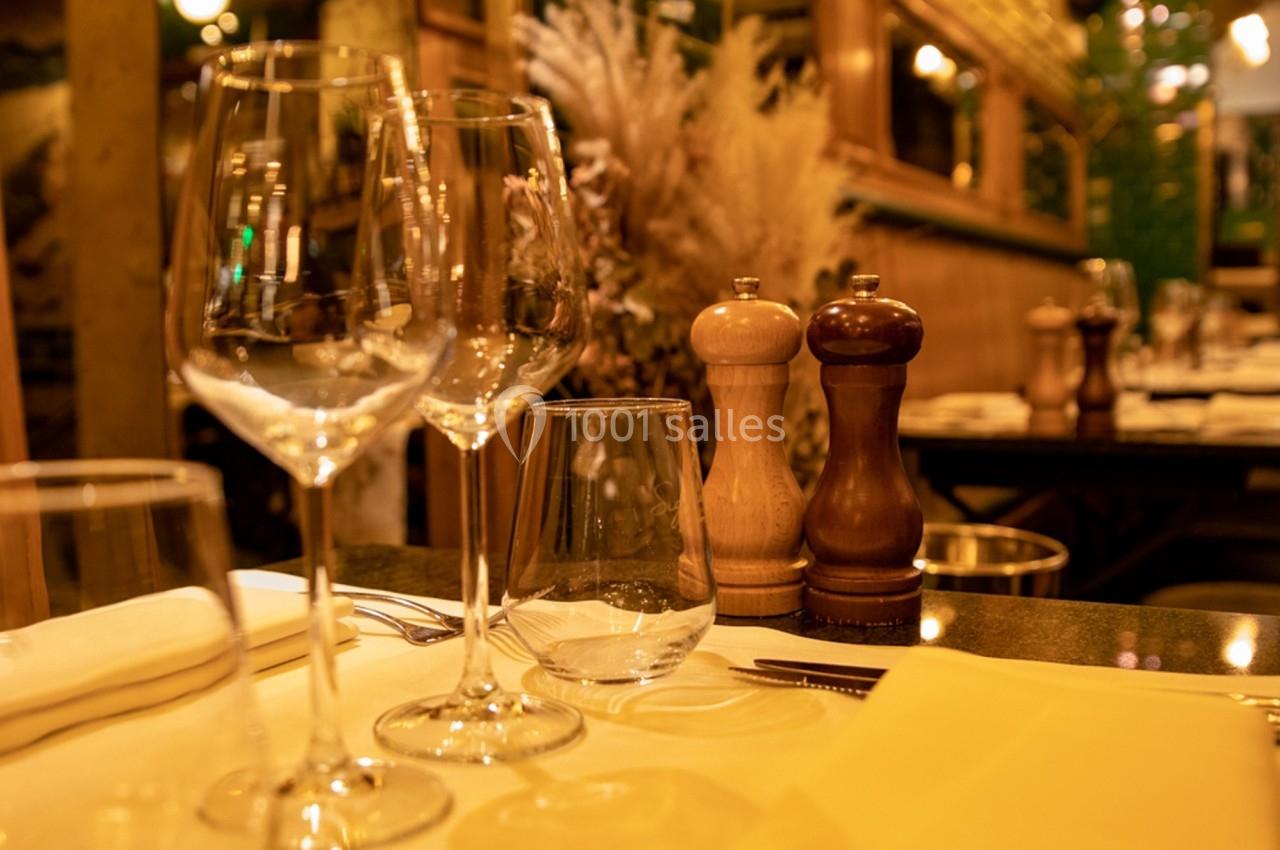 Table dressée avec des verres, couverts et serviettes, décorée de moulins à poivre dans un restaurant chaleureux.