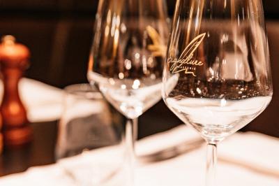 Salle de restaurant avec tables dressées, banquettes en bois, bar en bois et étagères garnies de verres et bouteilles.