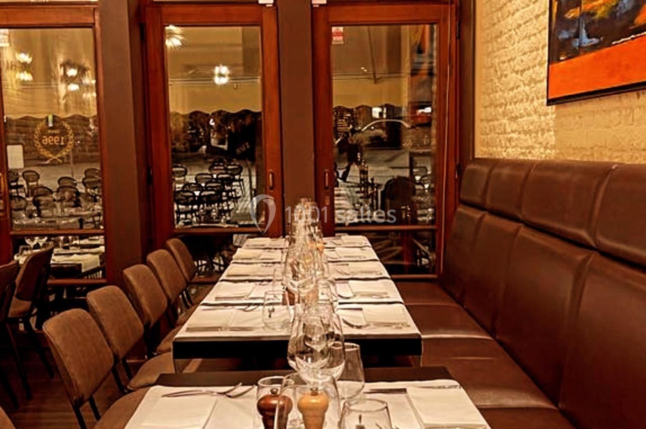 Salle de restaurant avec tables dressées, chaises alignées et grandes baies vitrées donnant sur l'extérieur.