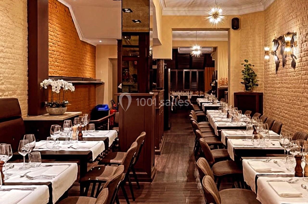 Salle de restaurant élégante avec tables dressées, murs en briques et éclairage chaleureux.