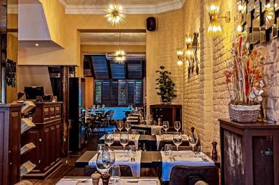 Salle de restaurant avec tables dressées, banquettes en bois, bar en bois et étagères garnies de verres et bouteilles.