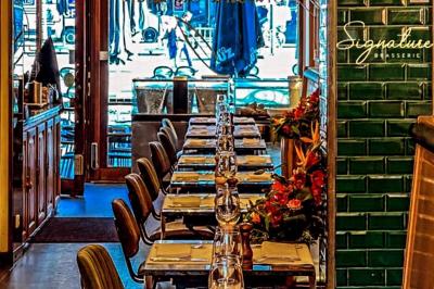 Salle de restaurant avec tables dressées, banquettes en bois, bar en bois et étagères garnies de verres et bouteilles.