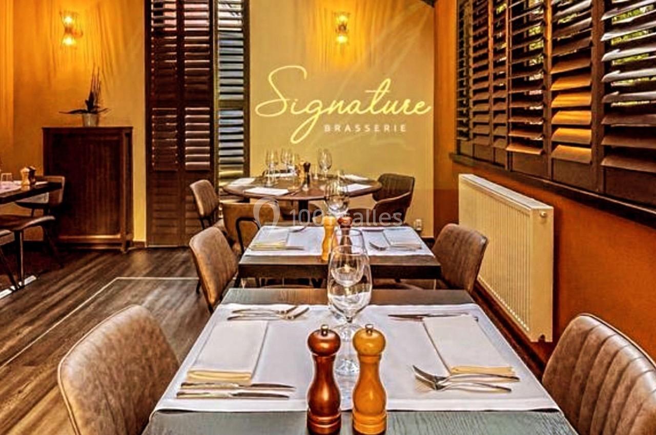 Salle de restaurant élégante avec tables dressées, lumière chaleureuse et logo ’Signature Brasserie’ sur un mur.