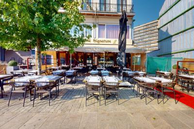 Salle de restaurant avec tables dressées, banquettes en bois, bar en bois et étagères garnies de verres et bouteilles.