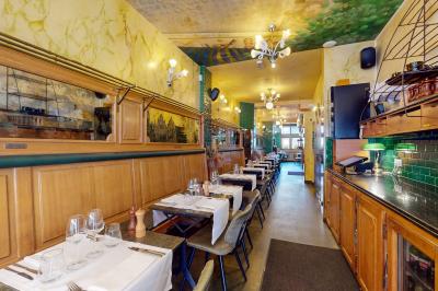 Salle de restaurant avec tables dressées, banquettes en bois, bar en bois et étagères garnies de verres et bouteilles.