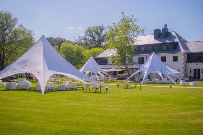Tentes blanches modernes installées sur une pelouse verte devant un bâtiment avec terrasse, par une journée ensoleillée.