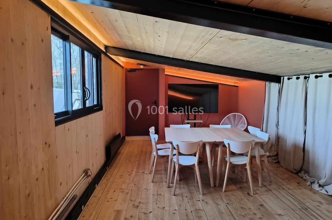 Salle de réunion avec table en bois, chaises blanches, écran mural et murs en bois et rouge.