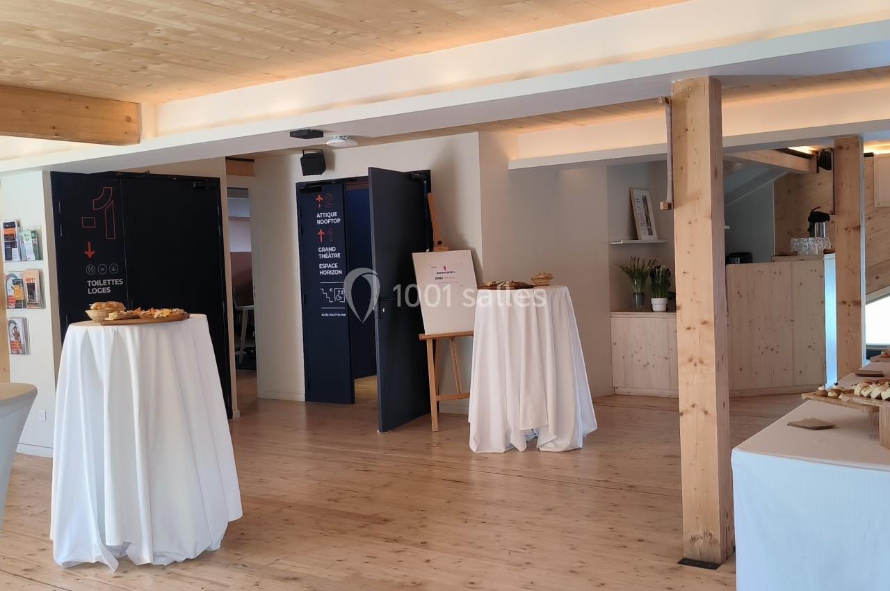 Salle lumineuse avec tables hautes nappées, buffet de viennoiseries et décor en bois clair.