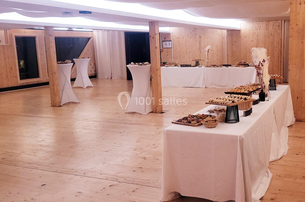 Salle en bois clair aménagée pour un buffet avec des tables dressées et des plateaux de nourriture.