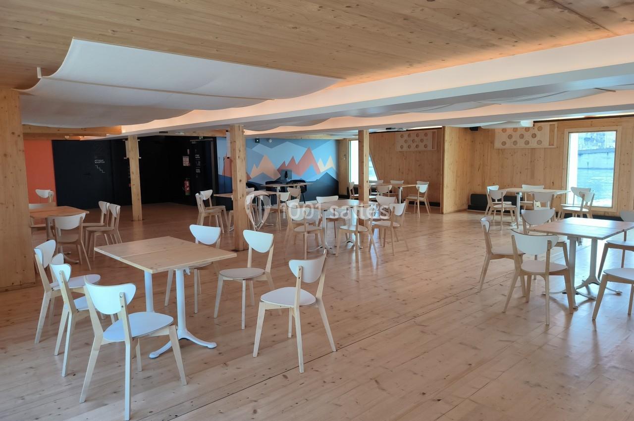 Salle lumineuse avec mobilier en bois clair, tables et chaises espacées, murs décorés de motifs géométriques.