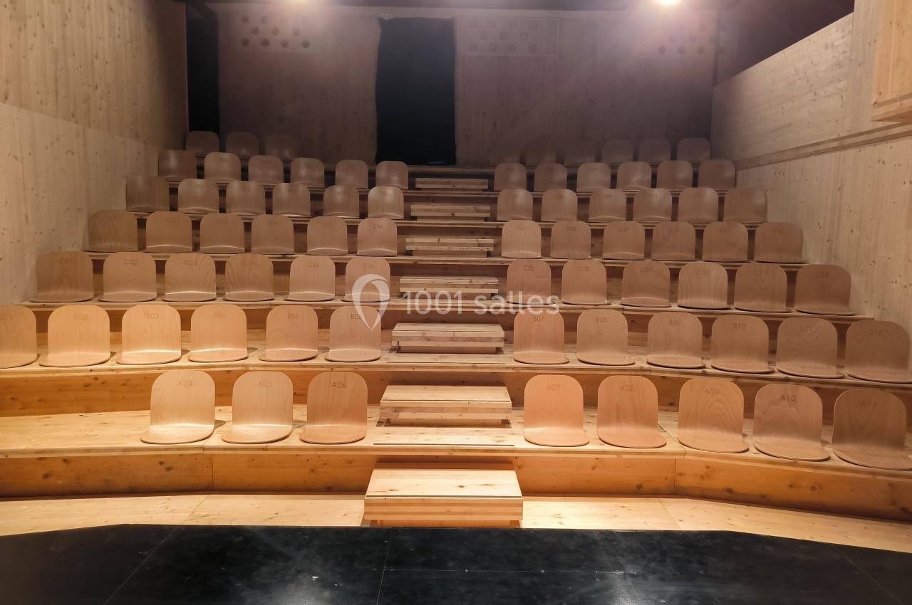 Gradins en bois clair avec des sièges alignés dans une petite salle au sol sombre et éclairée par des projecteurs.