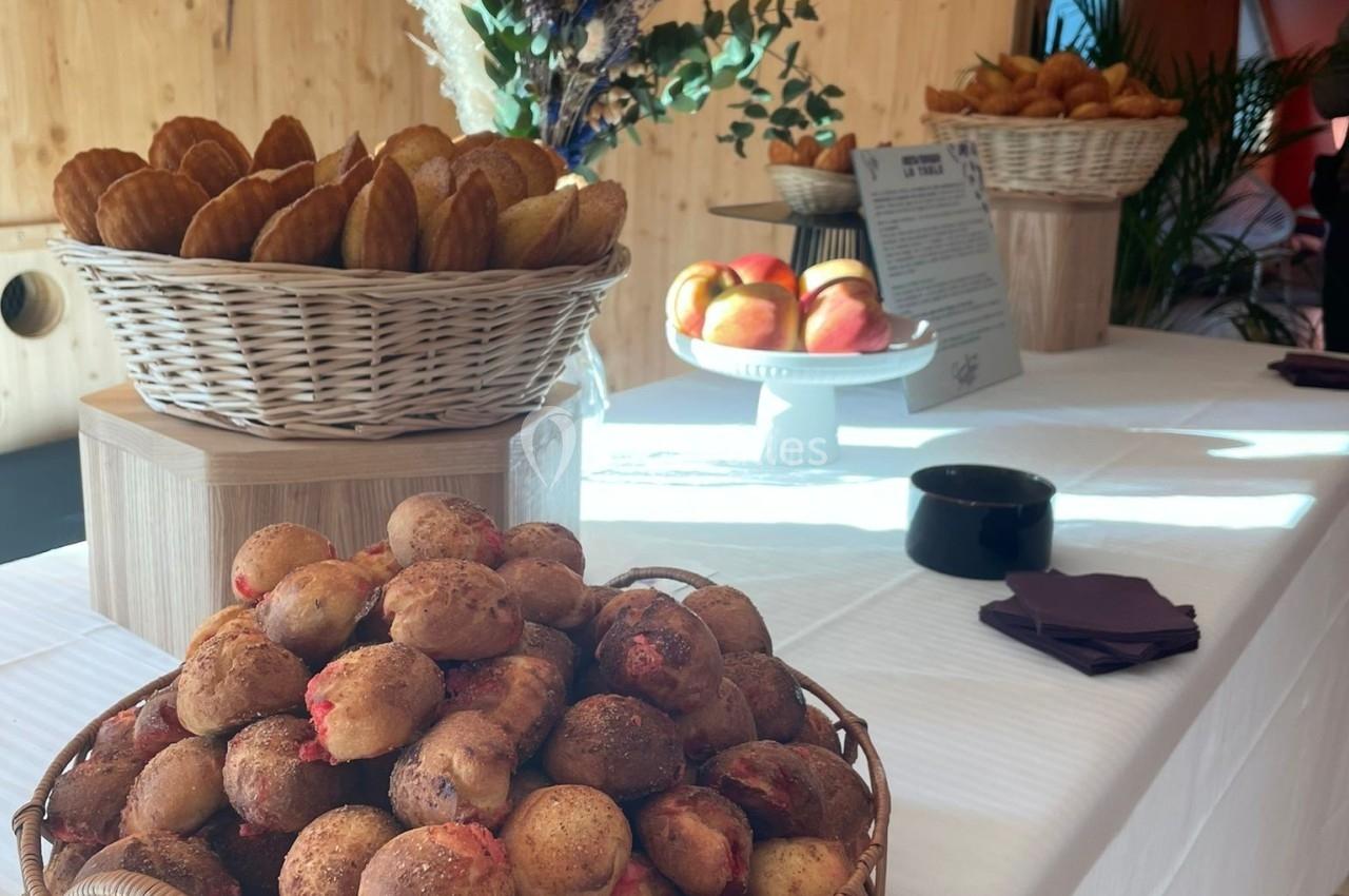 Table dressée avec des paniers de viennoiseries, pommes et décoration florale dans un espace en bois lumineux.