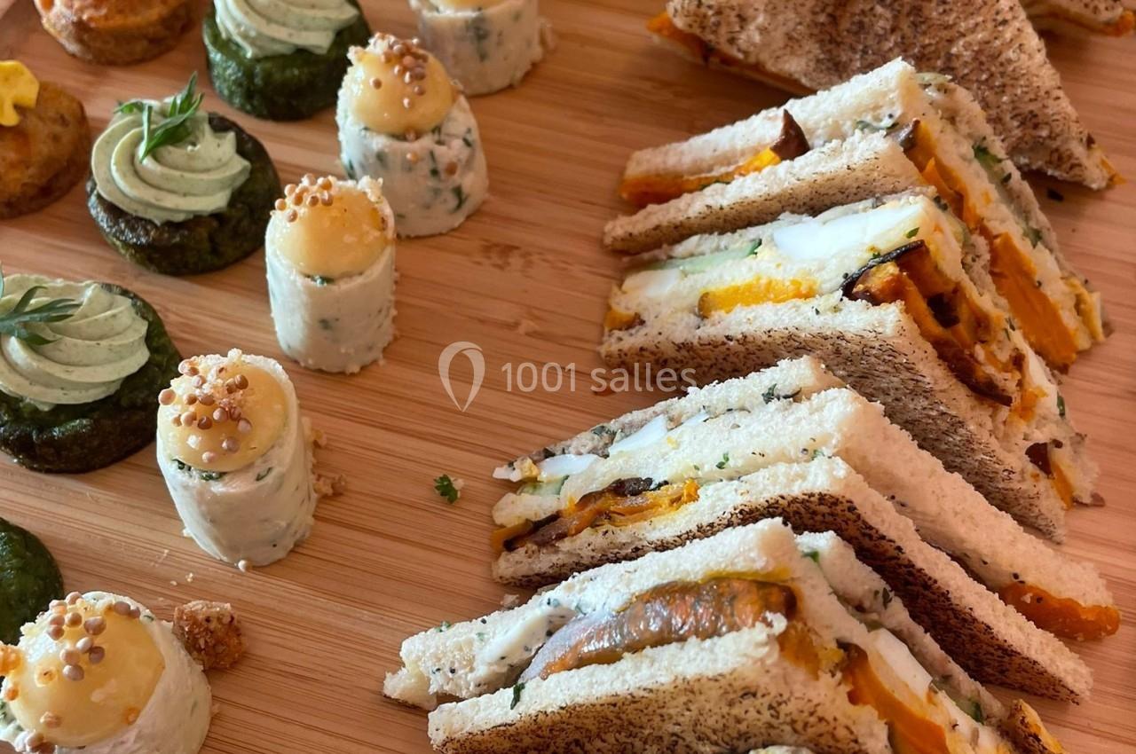 Plateau en bois avec des sandwichs triangulaires, des bouchées salées et des roulés garnis, disposés pour un apéritif.