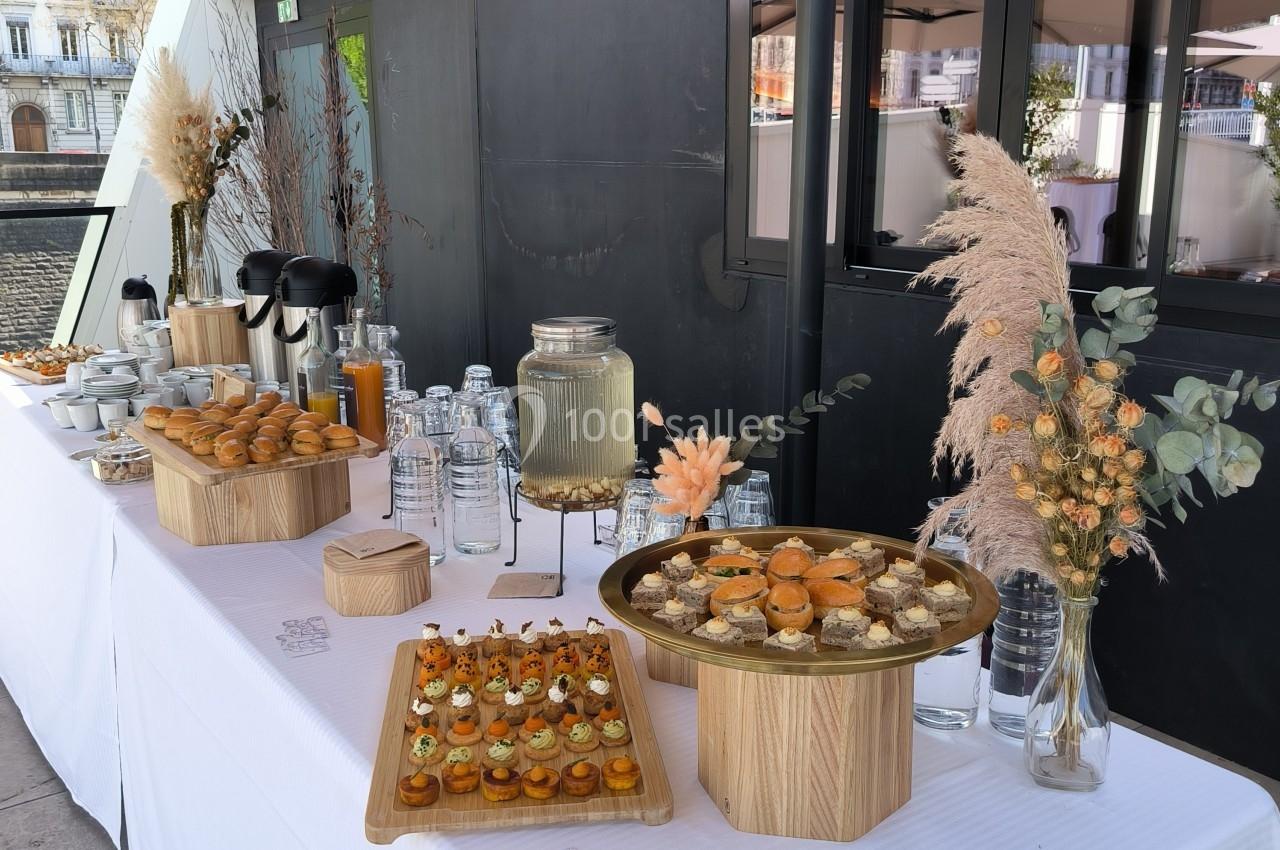 Buffet en extérieur avec boissons, verrines, pâtisseries et décorations florales sur une table blanche.