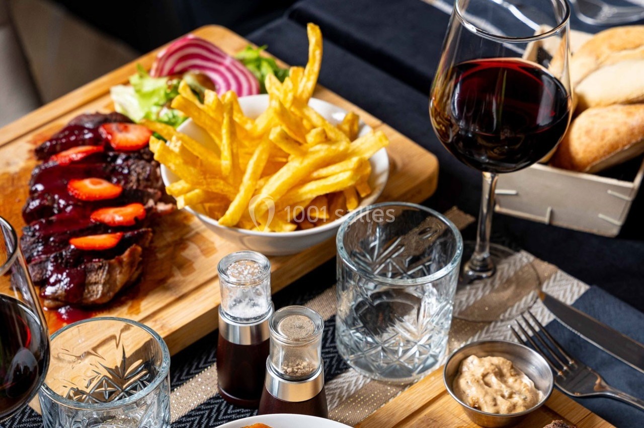 Assiette de steak avec sauce, frites, salade, accompagnée d'un verre de vin rouge et d'assaisonnements sur une table.