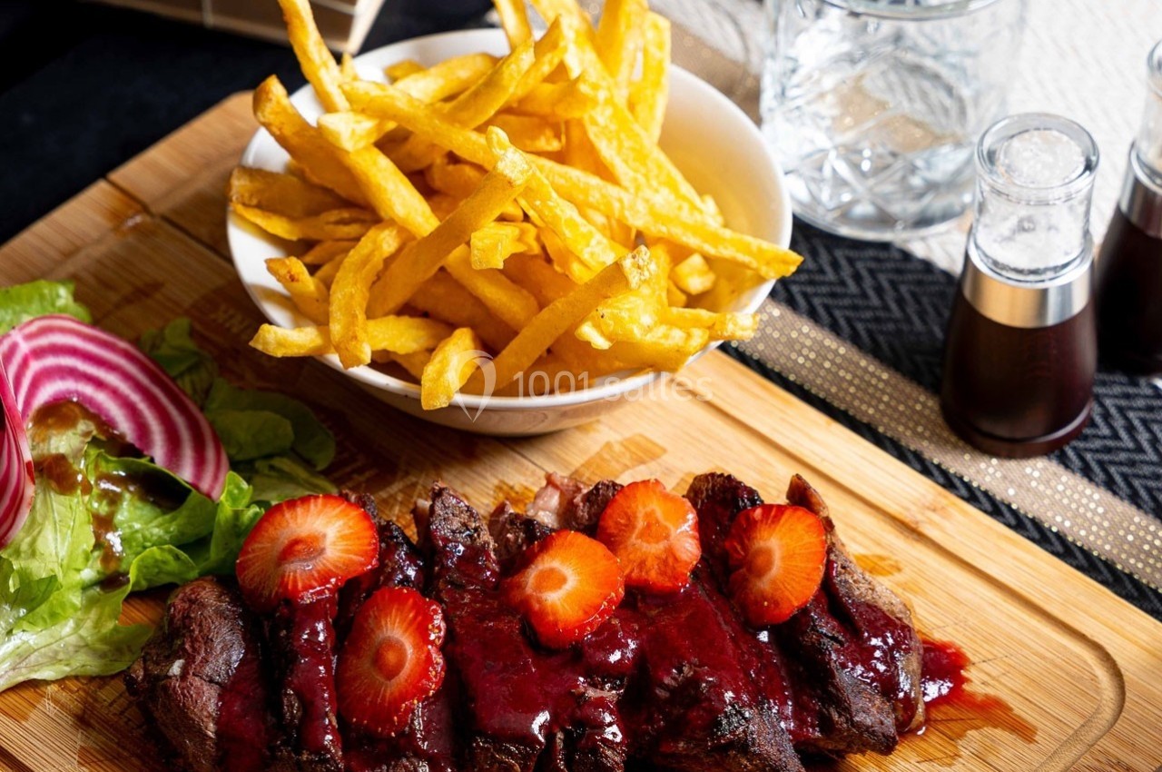 Assiette de viande nappée de sauce rouge avec des fraises, accompagnée de frites et d'une salade verte.