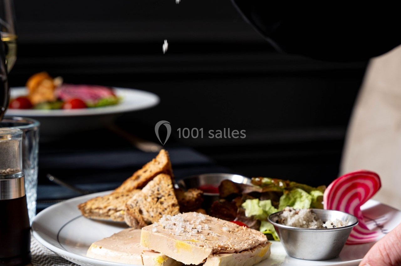 Assiette de foie gras avec toasts, salade, betterave et condiments, un geste saupoudre du sel au-dessus.