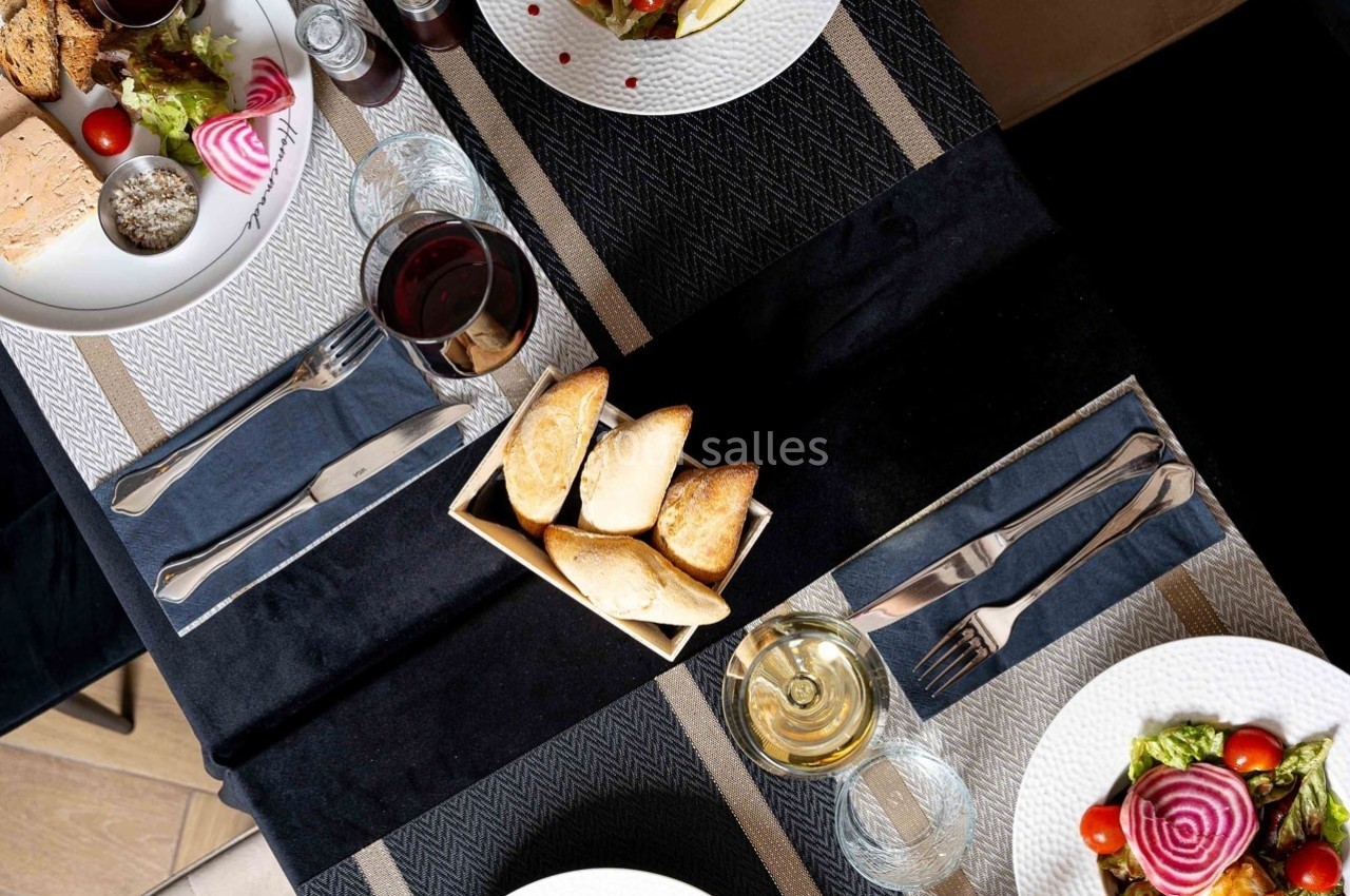 Table dressée avec des assiettes de salade, pain, verres de vin et couverts sur une nappe noire et beige.