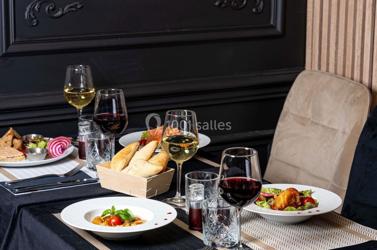 Table dressée avec des assiettes de plats variés, verres de vin rouge et blanc, et panier de pain dans un décor élégant.