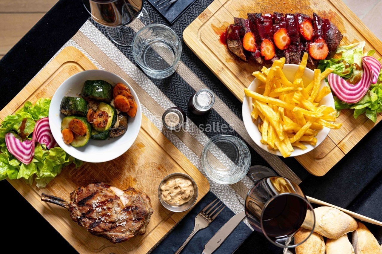 Repas composé de légumes grillés, côte de porc, frites, viande avec fraises, verres de vin et pain sur une table.