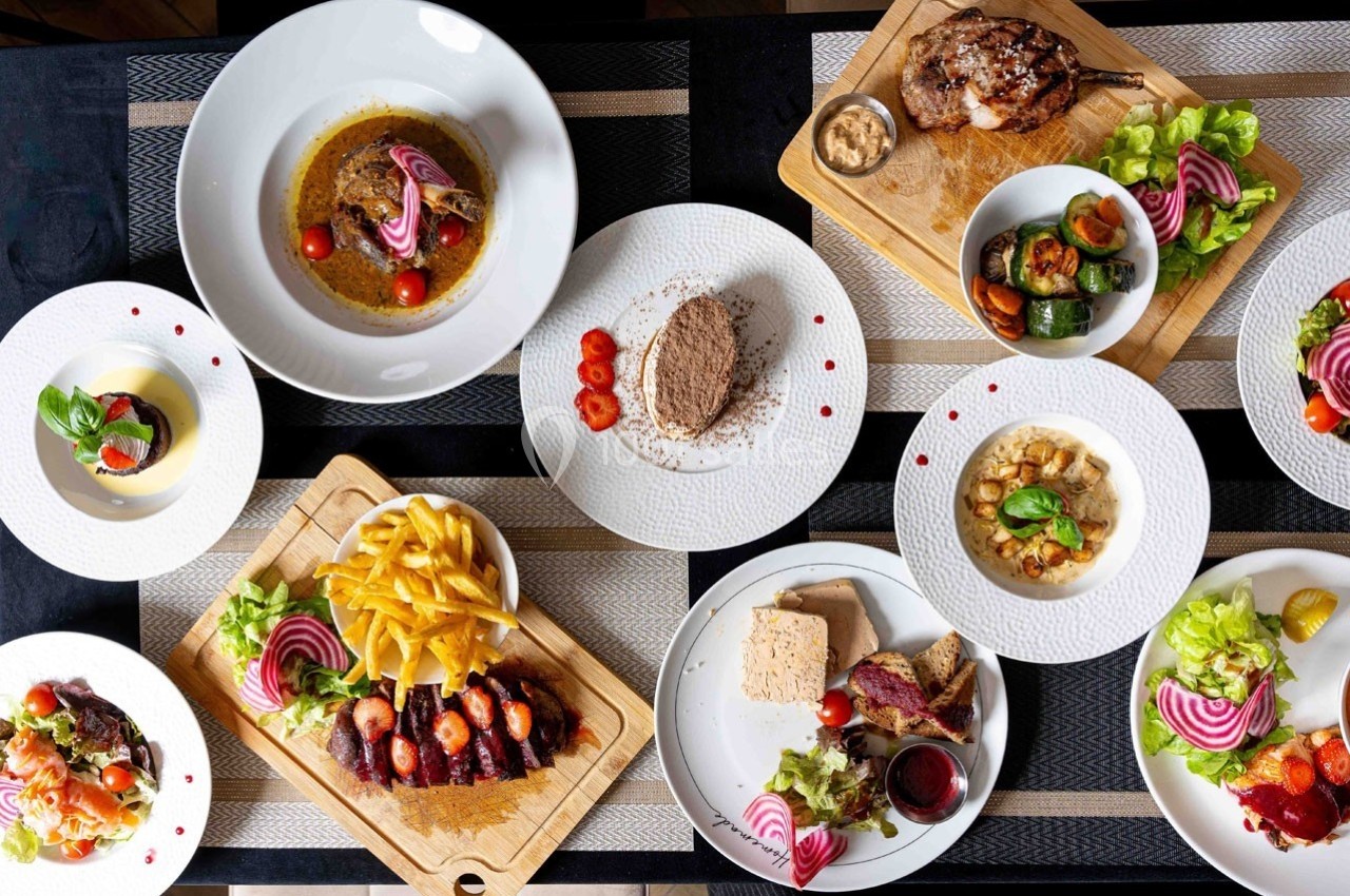 Vue de dessus d'une table dressée avec divers plats, incluant viandes, légumes, sauces et accompagnements.