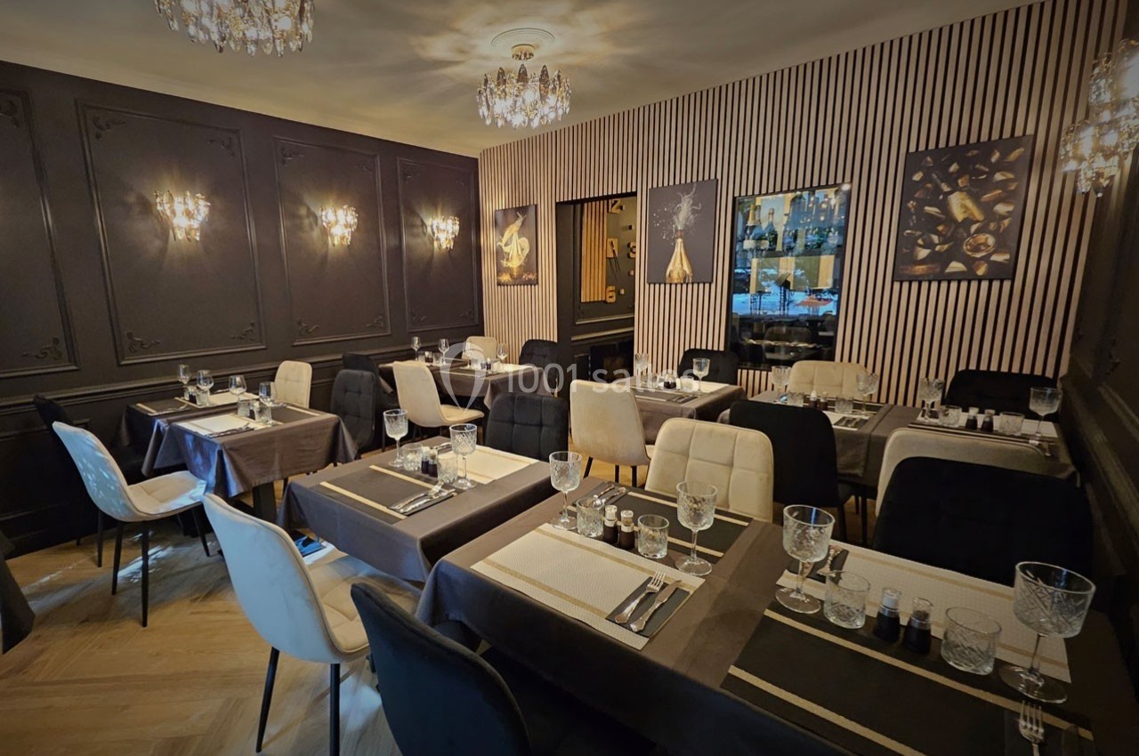 Salle de restaurant élégante avec tables dressées, chaises noires et blanches, éclairage chaleureux et décor raffiné.